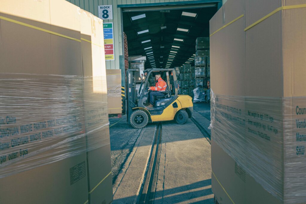 Image is taken between two pallets of stock while a fork lift turck drives past in the background