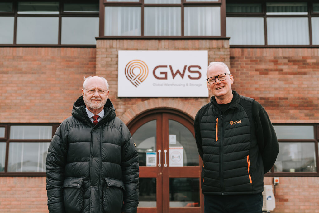 Two men stand outside of a brink building belonging to a warehouse and storage company