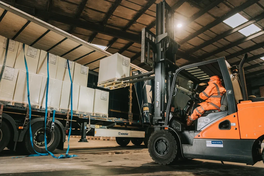 Forklift unloading boxed goods from a curtain-sided trailer in a GWS warehouse